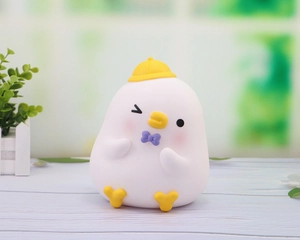 Detailed view of a white duck coin bank with yellow hat, purple bow, and winking face