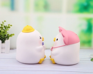 Detail of two cute vinyl duck piggy banks with colorful hats on a wooden surface