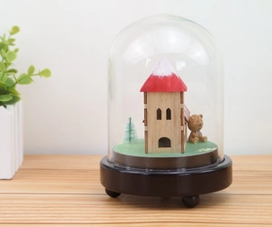 Close-up of wooden music box featuring a miniature house, Christmas tree, and teddy bear