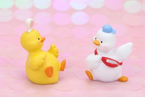 Cute resin duck figurines with bunny ears and blue cap on pink glitter background