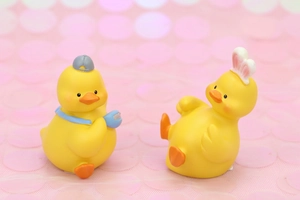 Detail of two cute yellow resin ducks with baseball cap and rabbit ears on pink sequins
