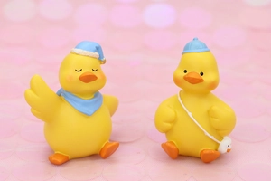Close-up of cute resin ducks with sleep hat and baseball cap on pink glitter background