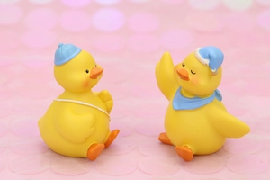 Detail shot of cute resin duck figurines with tiny blue hats and scarves on pink background