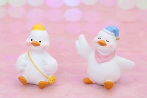 Cute resin duck figurines with tiny hats and scarves on a soft pink glitter background