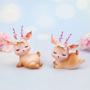Close-up of sleeping resin deer cake toppers with glitter antlers and floral detail