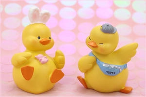 Detail view of two cute yellow resin ducks with a bunny ear hat and a blue Super bag