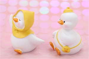 Primo piano di graziose statuine di anatre bianche con cappelli gialli su sfondo rosa