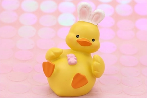 Close-up of yellow duck figurine with white bunny ears holding a small pink teddy bear