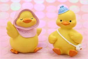 Close-up of cute cartoon duck figurines with hooded cloak and mini bag on pink bokeh background