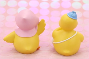 Rear view of two cute yellow duck ornaments with colorful hats on pink sequin background