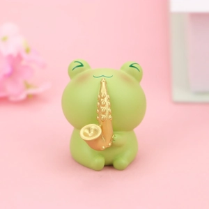 Niedliche grüne Froschfigur spielt goldenes Saxophon auf rosa Hintergrund Schreibtischdeko