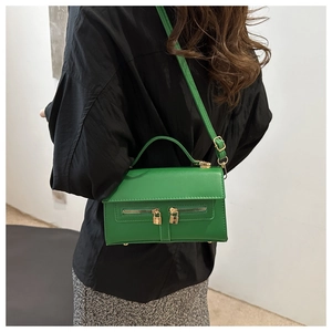 Detail of green leather handbag with dual zippers, gold locks and adjustable strap