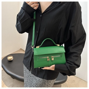 Close-up of bright green leather crossbody bag featuring gold hardware and double zippers