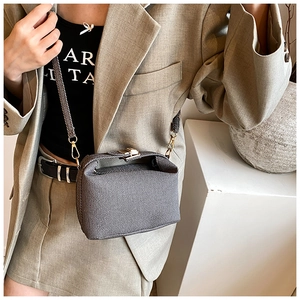 Close-up of a grey textured crossbody bag with a gold metal lock on a model outfit