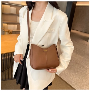 Close-up of brown leather tote bag with gold fashion lettering on a white blazer outfit