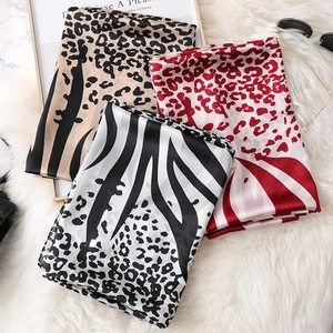 Detailed view of leopard and zebra print silk scarves folded on a soft white plush rug