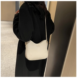 Close-up of white pebble leather crossbody bag on model, featuring fashion label detail