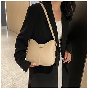 Detailed view of beige faux leather shoulder bag with FASHION metal hardware on a model