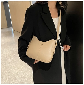 Detail of minimalist beige PU leather tote bag worn by a model in black blazer