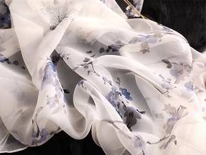 Detail of white silk scarf featuring elegant blue floral and butterfly patterns on fabric