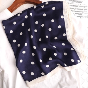 Détail du foulard en soie bleu marine à pois sur un t-shirt blanc et cintre en bois