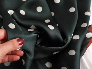 Gros plan sur foulard en soie vert foncé à pois montrant texture souple et éclat satiné