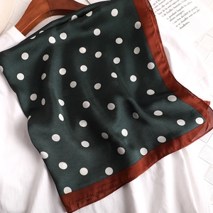 Gros plan d'un foulard en soie vert foncé à pois blancs avec bordure marron sur un cintre
