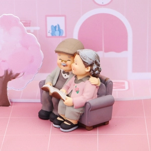 Elderly couple figurines sitting on a sofa reading, resin cake topper for anniversaries