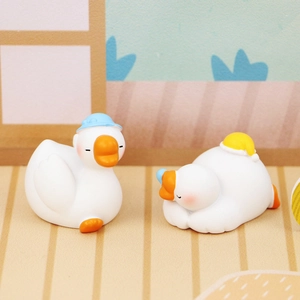 Close-up of cute mini resin white goose figurines in blue and yellow hats for car decor