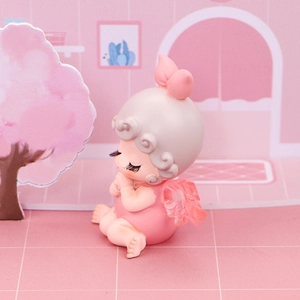 Gros plan d'une figurine de petit ange en prière avec des ailes roses pour gâteaux