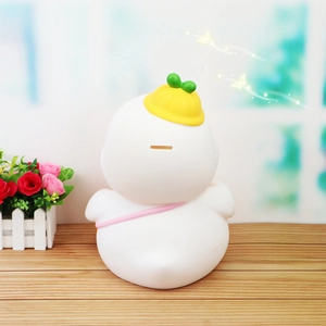 Back view of a white duck piggy bank with a yellow hat and pink strap on wood