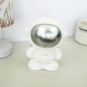 Astronaut piggy bank with silver visor and RICH emblem on a minimalist white desk