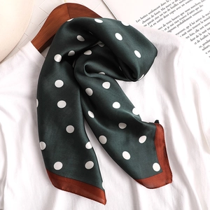 Détail du foulard en soie vert à pois blancs avec bordure caramel suspendu sur un cintre