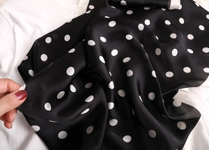 Gros plan d'un foulard en soie noir à pois blancs sur une chemise blanche