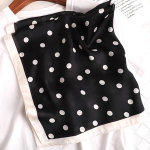 Détail d'un foulard en soie à pois noirs et blancs avec bordure crème sur un t-shirt