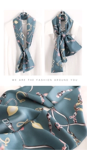 Detail of teal silk scarf with gold chain print and fringe on a white shirt