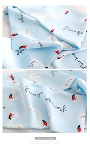 Close-up of light blue silk scarf fabric featuring white swan patterns and fringe detail