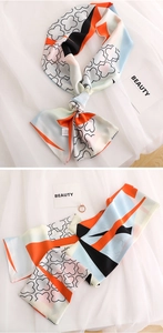 Close-up of long narrow silk scarf featuring orange clover patterns and tassel detail