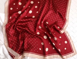 Close-up of red silk scarf featuring beige polka dots and smooth textured edges