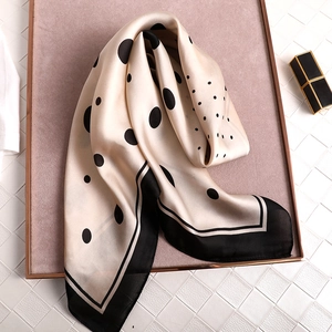 Elegant off-white silk scarf with black polka dots and border displayed on tray