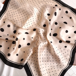 Detail of silk-like neck scarf showing beige fabric with black polka dots and satin texture