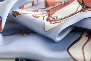 Detail of light blue silk scarf showing satin texture and equestrian saddle pattern