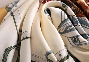 Detail of silk scarf showing equestrian buckle print and smooth satin texture with sheen