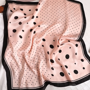 Vue détaillée d'un foulard en satin soyeux à pois noirs sur un fond orange pêche doux