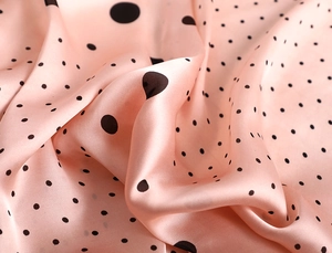 Détail d'un foulard en soie pêche à pois noirs montrant la texture satinée lisse