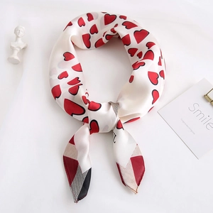Détail d'un foulard soyeux avec cœurs rouges et bordure géométrique sur fond blanc