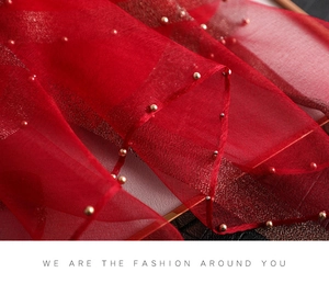 Detailed macro view of red semi-transparent silk scarf fabric with golden bead accents