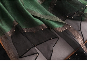 Close-up of silk scarf with emerald green fabric, sheer black mesh, and gold beaded trim