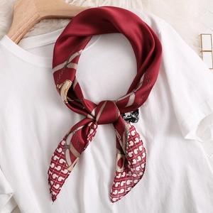 Détail d'un foulard en soie bordeaux avec motif chaîne dorée noué sur un t-shirt en coton