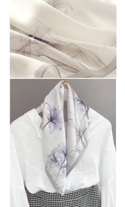 Detail of silk-like scarf featuring elegant lavender lily floral print and grey rolled edges